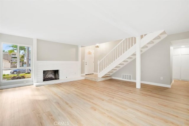 unfurnished living room featuring stairs, wood finished floors, visible vents, and a fireplace with raised hearth