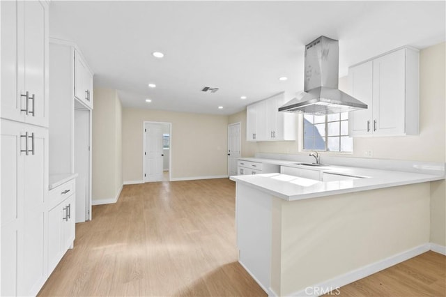 kitchen with baseboards, light countertops, light wood-style floors, island range hood, and a sink