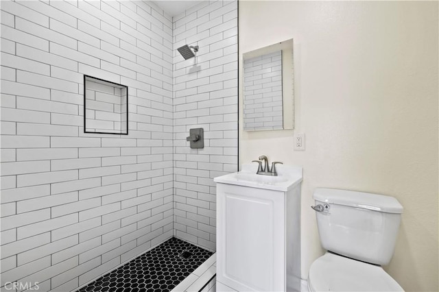 bathroom with a tile shower, toilet, and vanity