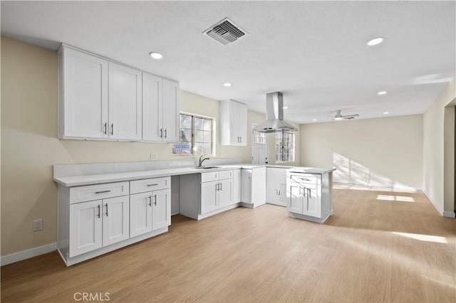 kitchen featuring visible vents, a peninsula, island range hood, white cabinets, and a sink