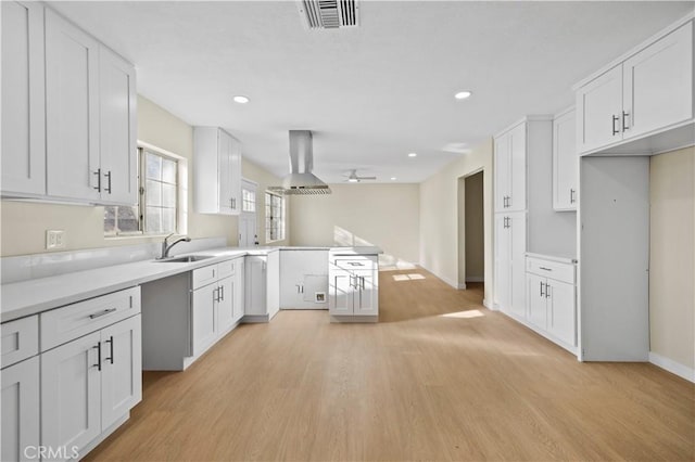 kitchen with light wood-style floors, a peninsula, exhaust hood, and white cabinetry