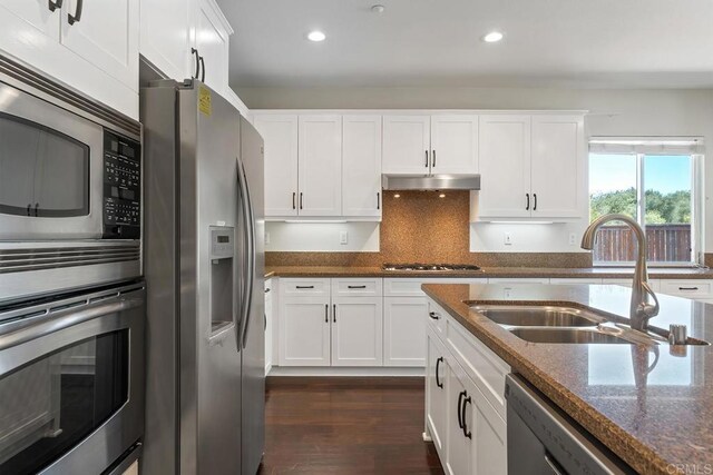 kitchen featuring a sink, under cabinet range hood, white cabinetry, stainless steel appliances, and dark stone counters