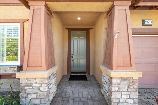 view of exterior entry featuring stucco siding, stone siding, and an attached garage