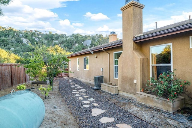 view of side of property with a garden, stucco siding, a chimney, and fence