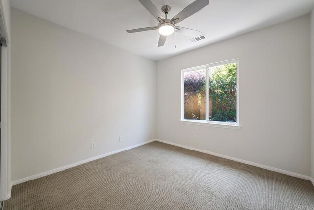 carpeted spare room with visible vents, a ceiling fan, and baseboards