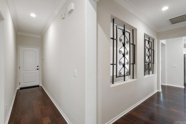 hall featuring visible vents, crown molding, baseboards, and wood finished floors