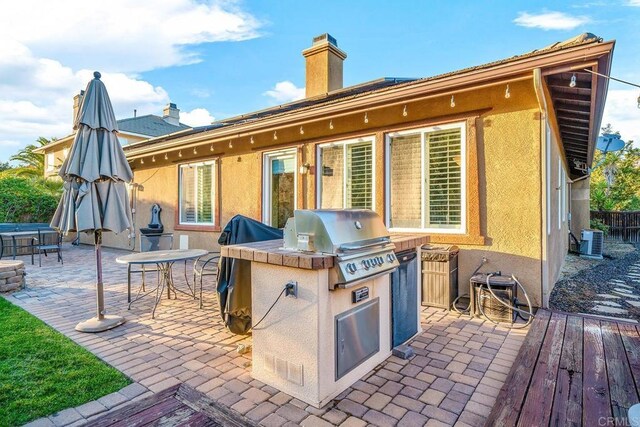 back of house featuring exterior kitchen, central AC unit, stucco siding, a chimney, and a patio