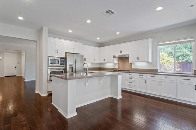 kitchen featuring visible vents, under cabinet range hood, a sink, stainless steel appliances, and dark stone counters