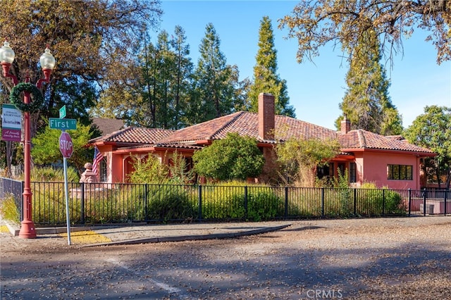 view of front facade with a fenced front yard, stucco siding, a tiled roof, and a chimney