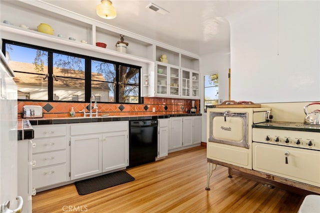 kitchen with visible vents, a sink, tile counters, white cabinets, and black dishwasher