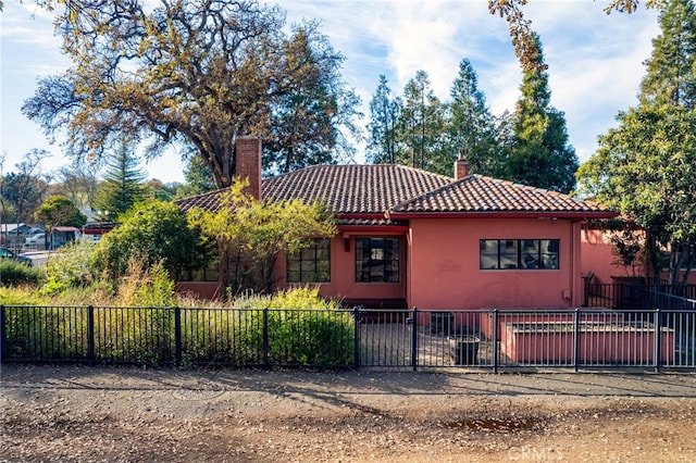 mediterranean / spanish-style home featuring fence private yard, stucco siding, a tiled roof, and a chimney