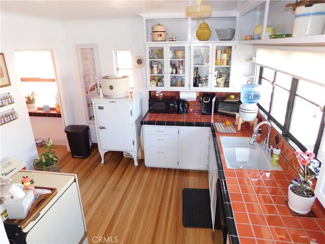 kitchen with a sink, a wealth of natural light, tile counters, and white cabinetry