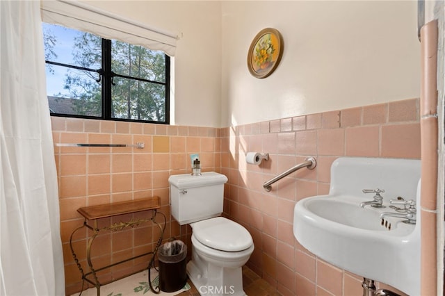 bathroom with a wainscoted wall, toilet, tile walls, and a sink