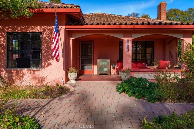 view of exterior entry with covered porch, stucco siding, and a tile roof