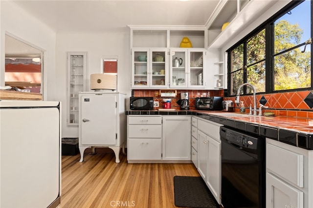 kitchen featuring black appliances, a sink, light wood-style floors, white cabinets, and tile counters