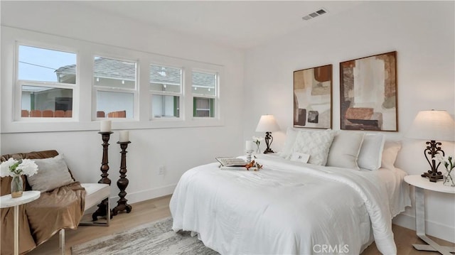 bedroom with multiple windows, wood finished floors, visible vents, and baseboards