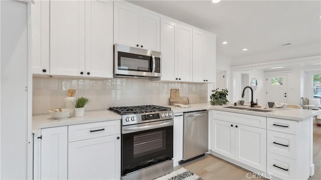 kitchen featuring a sink, stainless steel appliances, a peninsula, light countertops, and decorative backsplash