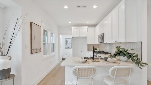 kitchen featuring visible vents, a peninsula, light countertops, white cabinetry, and stainless steel microwave