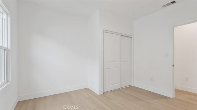 unfurnished bedroom featuring baseboards, visible vents, a closet, and light wood-type flooring