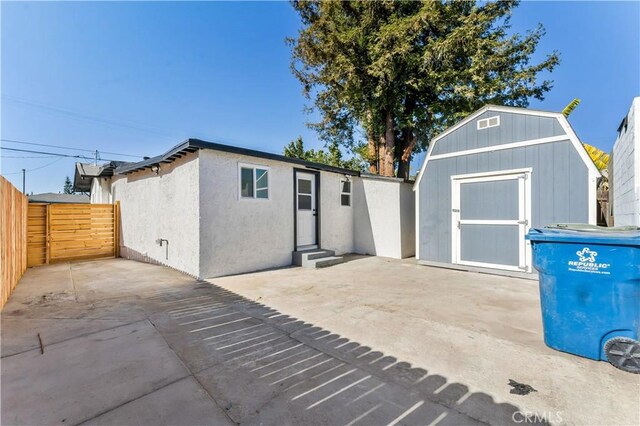 exterior space with fence, a gambrel roof, an outdoor structure, a patio area, and a storage unit