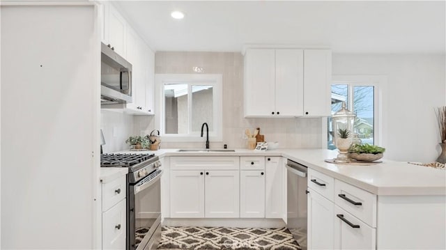 kitchen featuring a peninsula, a sink, light countertops, white cabinets, and appliances with stainless steel finishes