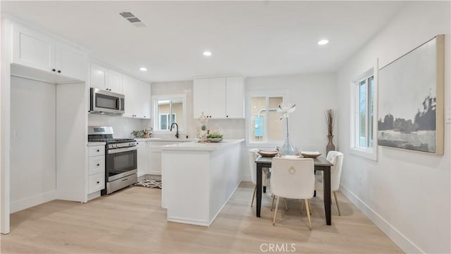 kitchen featuring light wood-style flooring, white cabinetry, stainless steel appliances, and light countertops