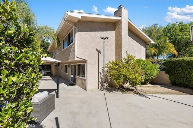 view of home's exterior featuring a patio, a chimney, and stucco siding