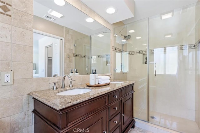 full bath featuring double vanity, a stall shower, tile walls, and a sink