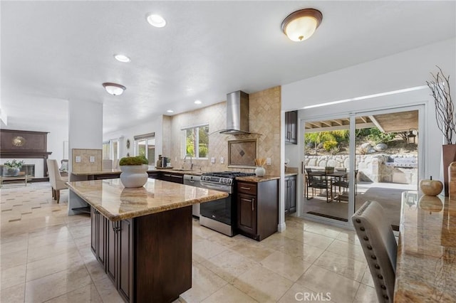 kitchen featuring a sink, decorative backsplash, wall chimney range hood, and stainless steel gas range oven