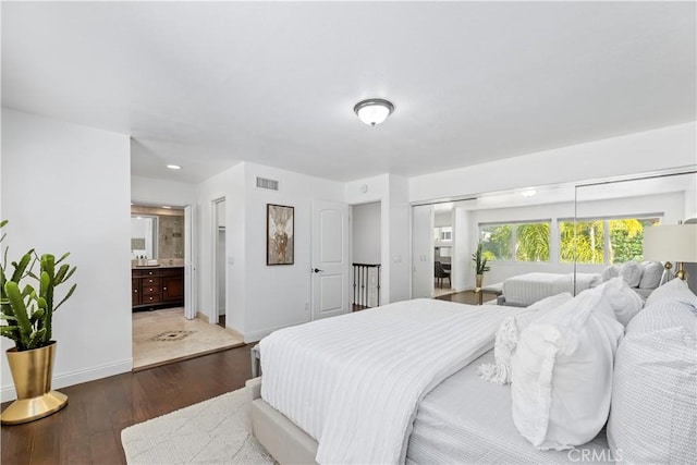 bedroom with visible vents, ensuite bathroom, baseboards, and wood finished floors