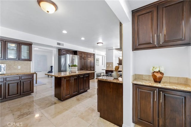 kitchen featuring light stone counters, a kitchen island, stainless steel appliances, decorative backsplash, and dark brown cabinets