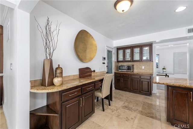 interior space featuring stainless steel microwave, glass insert cabinets, tasteful backsplash, and dark brown cabinets