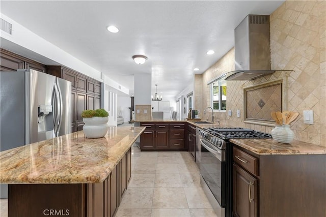 kitchen with light stone counters, stainless steel appliances, backsplash, and wall chimney range hood