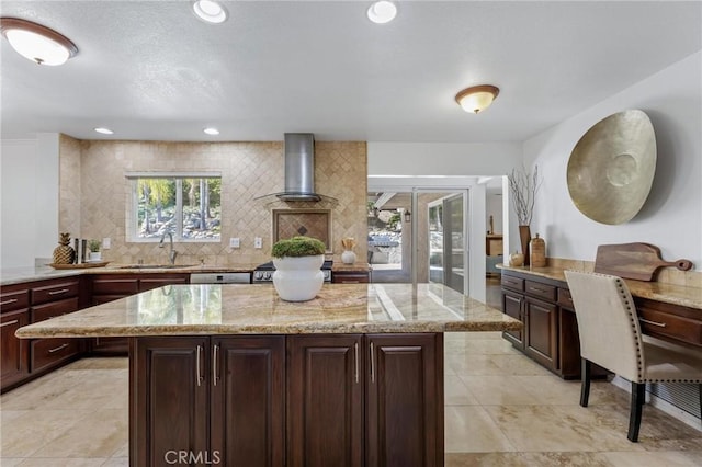 kitchen with a sink, light stone counters, tasteful backsplash, and wall chimney range hood