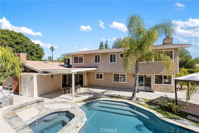 rear view of property featuring an in ground hot tub, an outdoor pool, stucco siding, a chimney, and a patio area