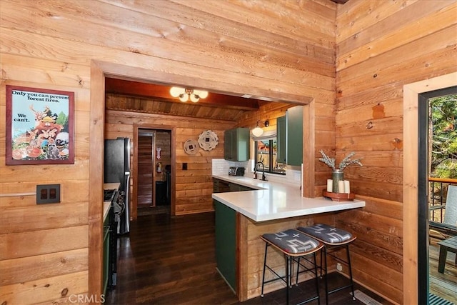 kitchen with wood walls, light countertops, a peninsula, a kitchen breakfast bar, and a sink