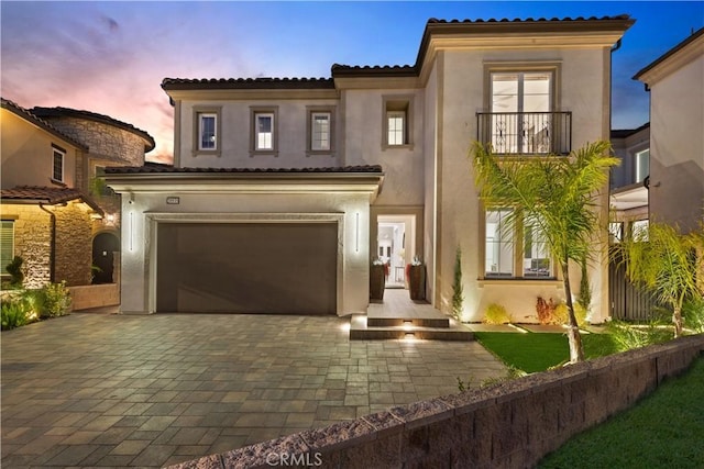 mediterranean / spanish house with a garage, stucco siding, decorative driveway, and a balcony