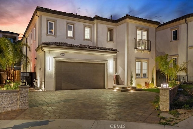 mediterranean / spanish home featuring stucco siding, an attached garage, a tile roof, and decorative driveway