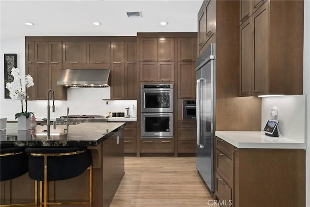 20535 W Bluebird Ct, Porter Ranch, CA 91326 - kitchen with under cabinet range hood, appliances with stainless steel finishes, light wood-style floors, a breakfast bar, and recessed lighting