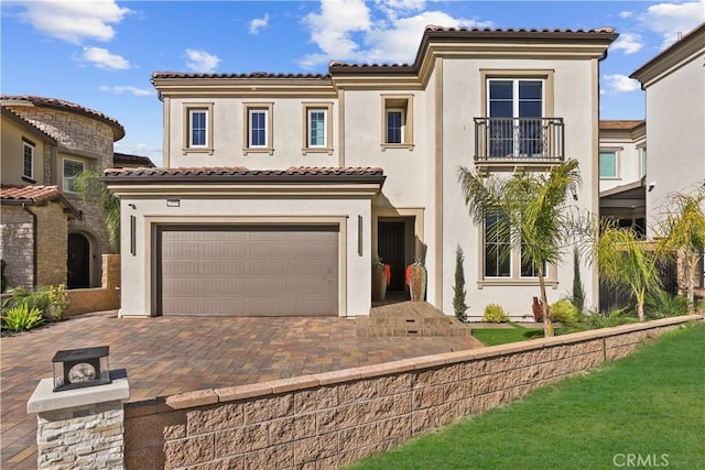 mediterranean / spanish-style house featuring stucco siding, decorative driveway, a garage, a balcony, and a tiled roof