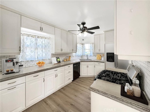 kitchen with range with gas stovetop, light wood-style flooring, a sink, black dishwasher, and tasteful backsplash