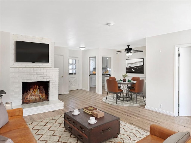 living area featuring baseboards, ceiling fan, a fireplace, and light wood finished floors