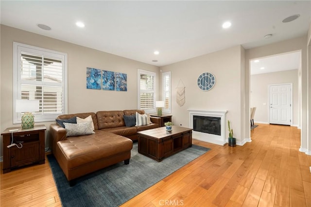 living area featuring recessed lighting, baseboards, a glass covered fireplace, and light wood finished floors