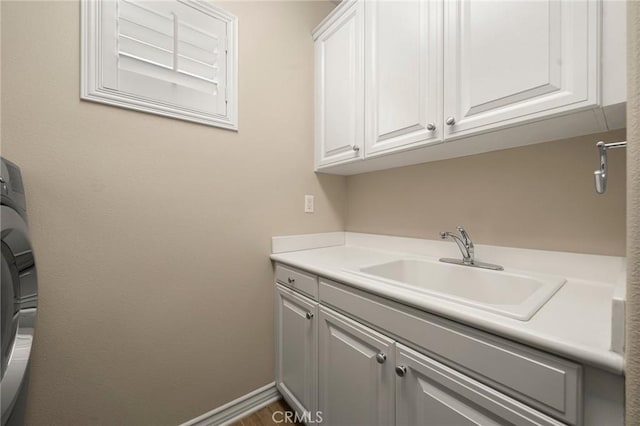 laundry room featuring a sink, baseboards, cabinet space, and washer / clothes dryer