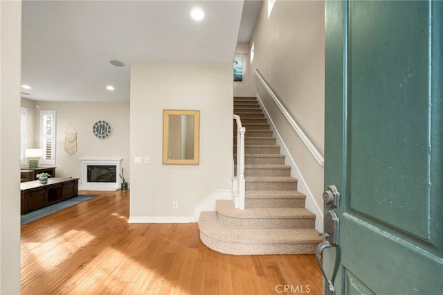 foyer entrance featuring baseboards, stairway, recessed lighting, hardwood / wood-style flooring, and a glass covered fireplace