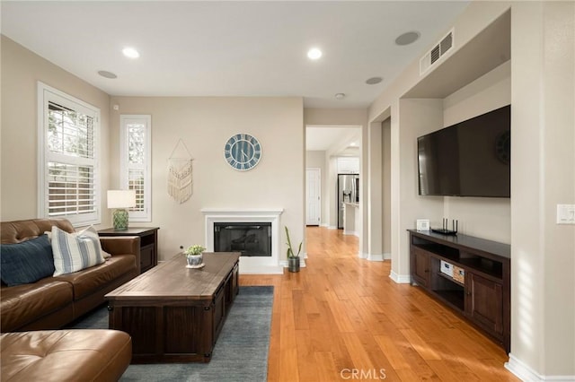 living room with visible vents, a glass covered fireplace, recessed lighting, light wood finished floors, and baseboards