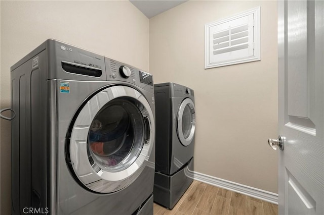 laundry area with laundry area, washing machine and dryer, baseboards, and light wood finished floors