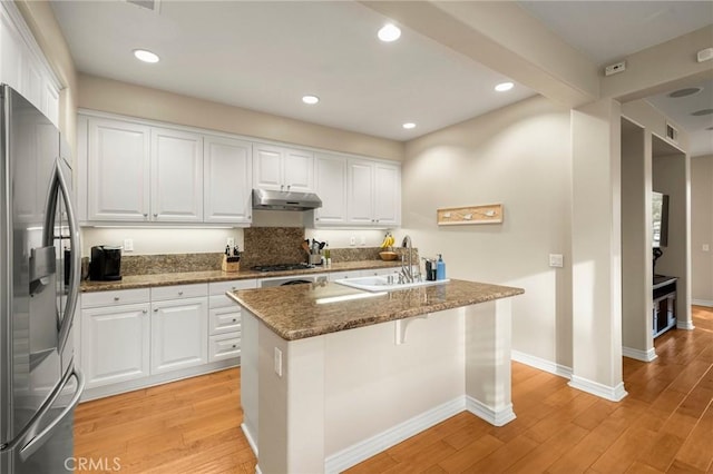 kitchen with light wood finished floors, under cabinet range hood, stainless steel fridge, white cabinetry, and a sink