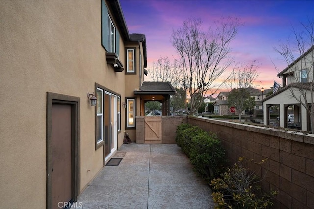 view of side of home featuring a patio area, stucco siding, fence, and a gate