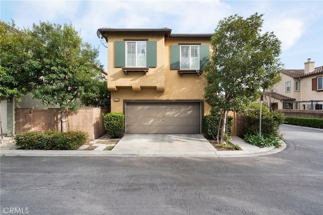 view of front of house with concrete driveway, an attached garage, fence, and stucco siding